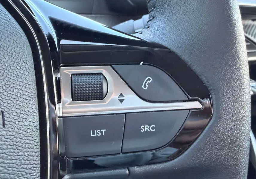 Gros plan sur les commandes audio au volant noir brillant d'une Peugeot 208 jaune, boutons LIST, SRC et téléphone.