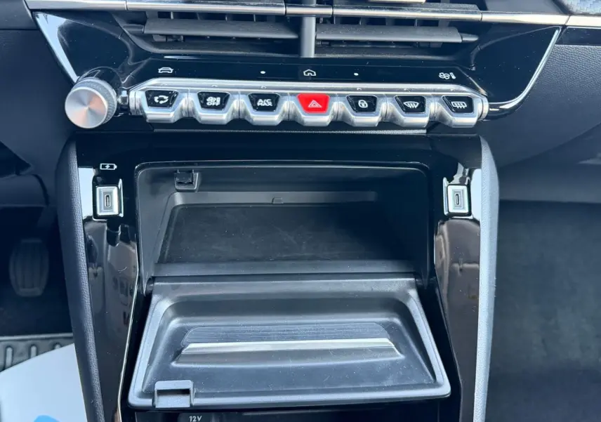 Vue rapprochée de la console centrale noire brillante de la Peugeot 208 1.2 100ch, avec commandes et rangement ouvert.