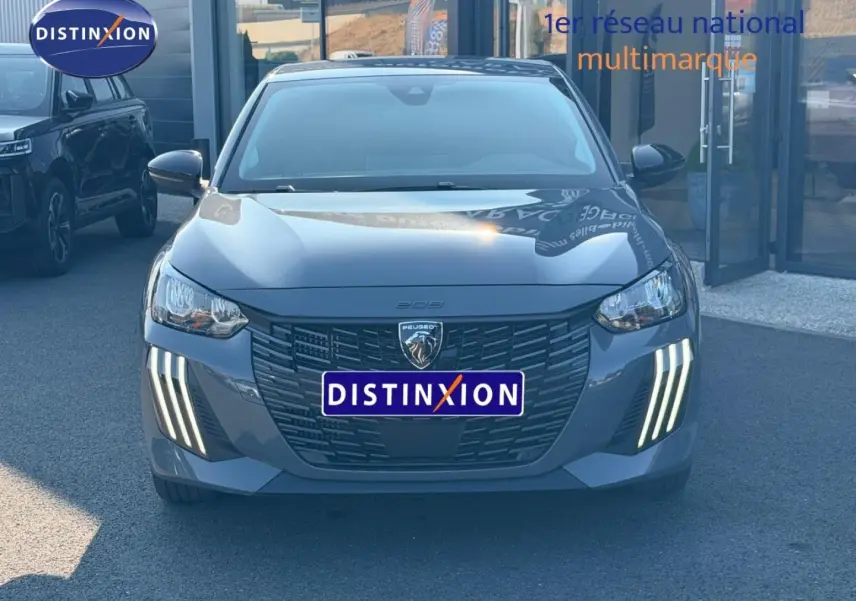 Vue frontale d'une Peugeot 208 grise avec feux LED verticaux allumés, calandre noire et logo lion central.
