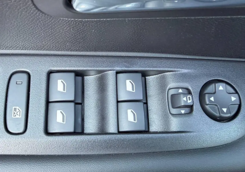 Gros plan sur les commandes électriques des vitres et des rétroviseurs côté conducteur d'une Peugeot 208 jaune 2025.