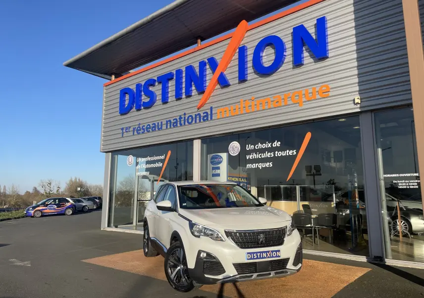 Peugeot 3008 blanc nacré vue 3/4 avant droit devant un showroom Distinxion par temps ensoleillé.