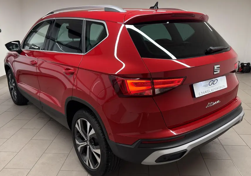 Vue 3/4 arrière droite du SEAT Ateca 2024 Rouge Velvet avec jantes alliage et feux LED allumés dans un garage.