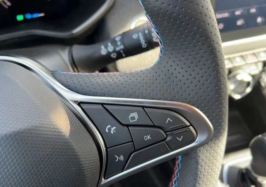 Gros plan sur les commandes du volant en cuir perforé noir avec surpiqûres tricolores de la Renault Clio V E-Tech 145 Esprit Alpine.