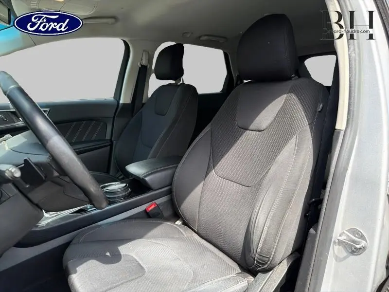 Vue intérieure côté conducteur du Ford Edge gris Ingot de 2016, mettant en valeur les sièges sport en tissu noir et l'accoudoir central.
