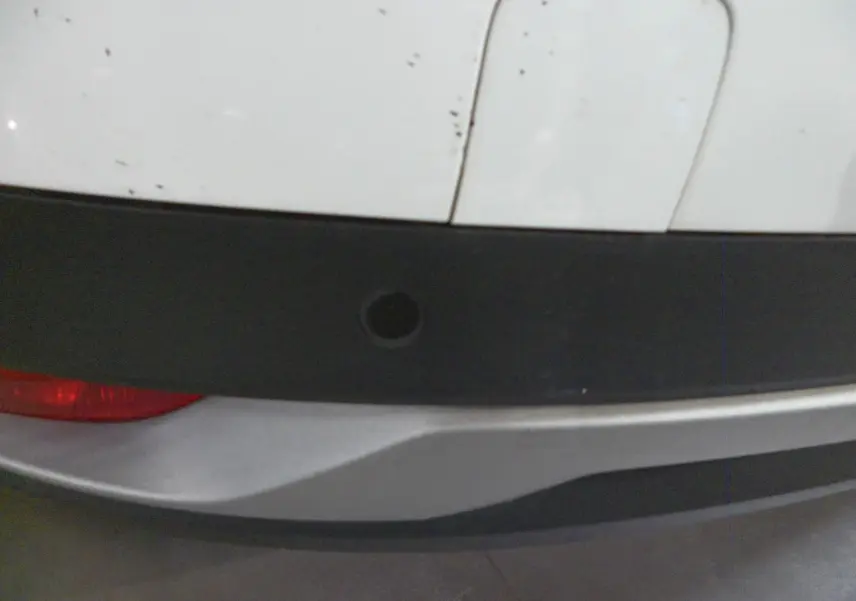 Gros plan sur le pare-chocs arrière blanc glacier du Renault Grand Scenic IV avec capteur de recul noir visible.