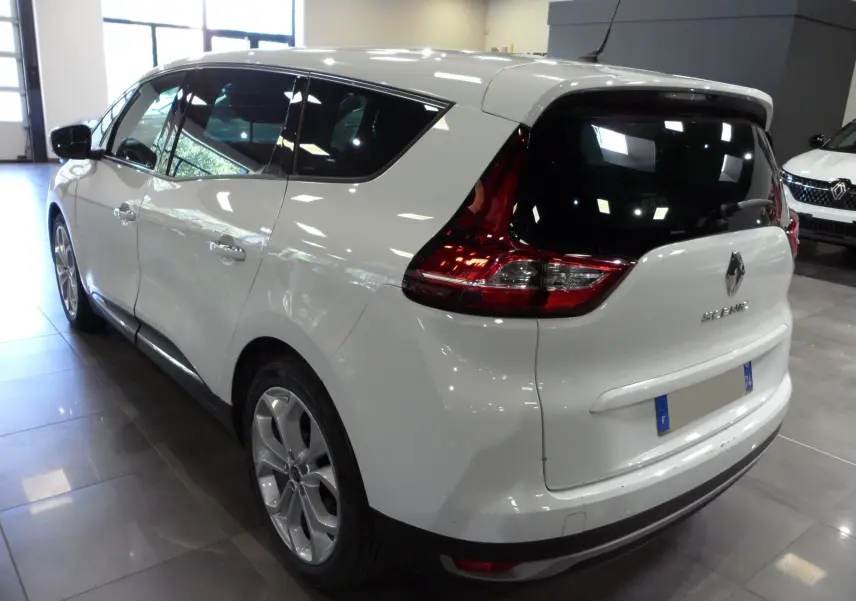 Renault Grand Scenic IV blanc glacier vu en 3/4 arrière droit dans un showroom lumineux.
