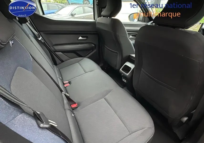 Vue intérieure arrière du Dacia Duster blanc Arctic 2025, sièges noirs en tissu avec ceintures de sécurité visibles.