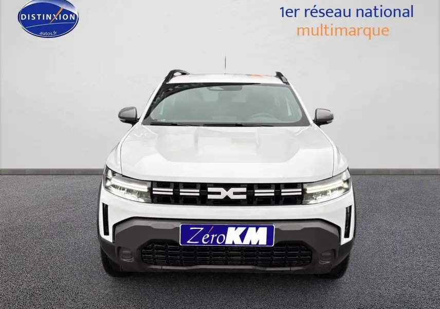 Vue frontale d'un Dacia Duster blanc arctic avec calandre noire et phares LED allumés sur fond neutre.