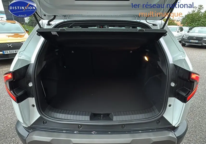 Coffre ouvert vu de l'arrière d'un Dacia Duster blanc Arctic avec feux arrière allumés sur parking.
