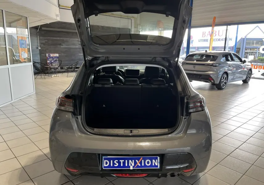 Vue arrière avec coffre ouvert d'une Peugeot 208 1.2 essence gris clair Selenium en showroom.