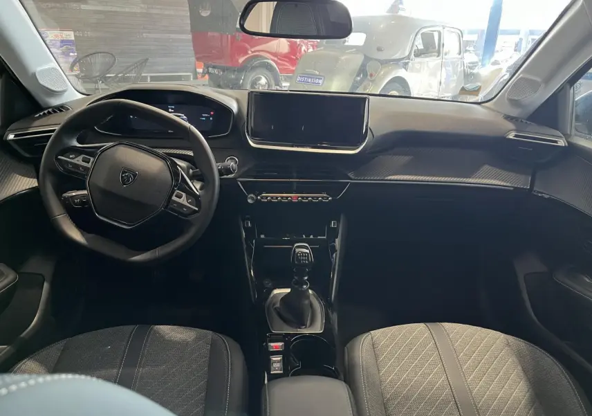 Intérieur Peugeot 208 2024 vu de face, volant cuir, tableau de bord numérique et levier de vitesse manuel.