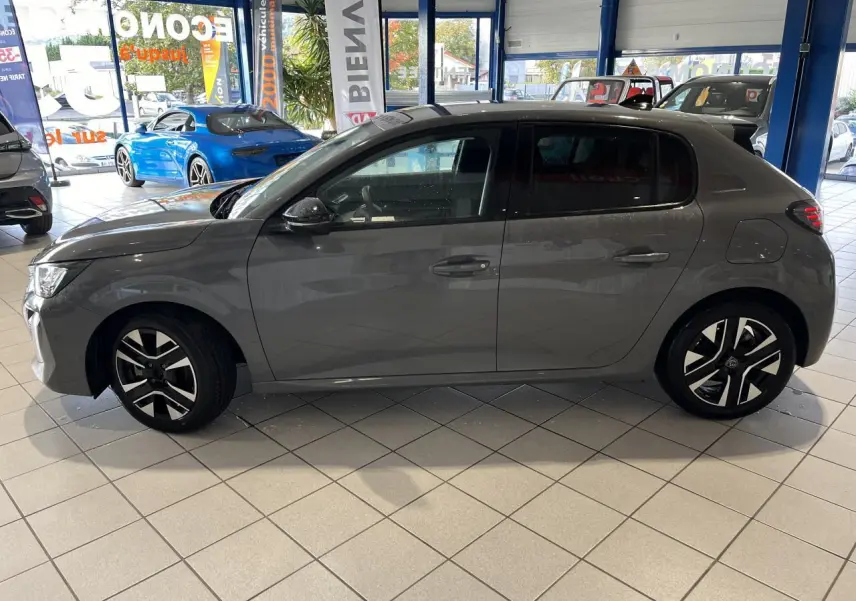 Profil côté gauche de la Peugeot 208 1.2 essence gris clair Selenium avec jantes alliage diamantées en showroom.