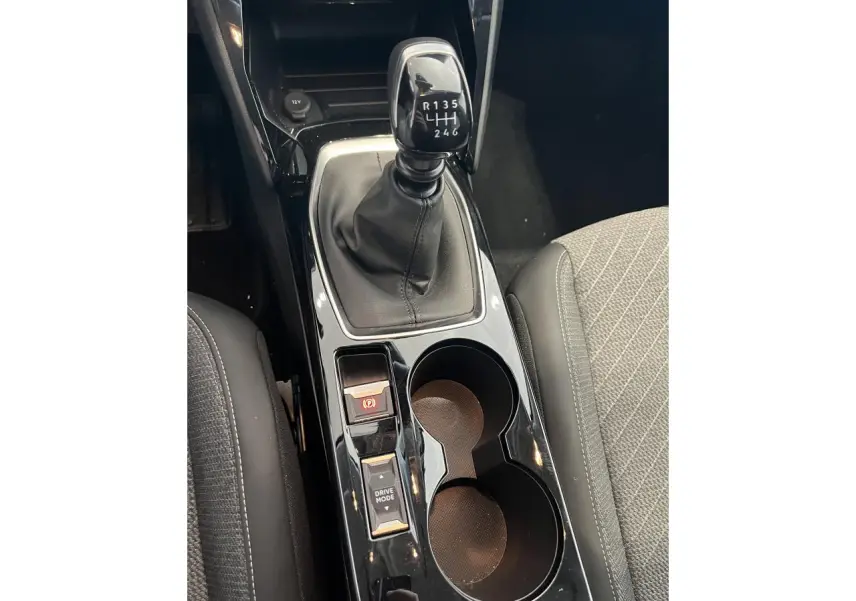 Vue rapprochée de la console centrale noire brillante avec levier de vitesse manuelle et porte-gobelets dans une Peugeot 208 gris clair.