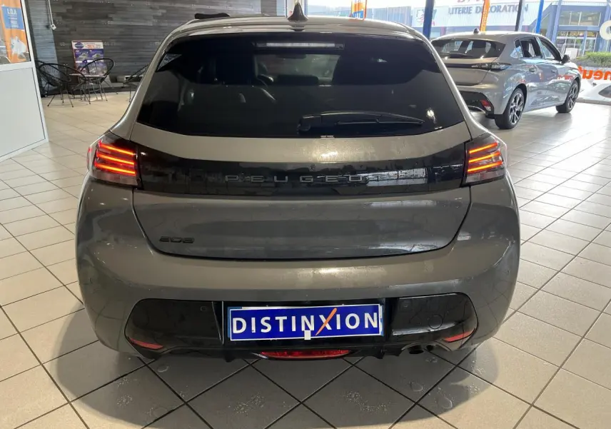 Vue arrière d'une Peugeot 208 gris clair Selenium avec feux arrière à LED et bandeau noir brillant en concession.