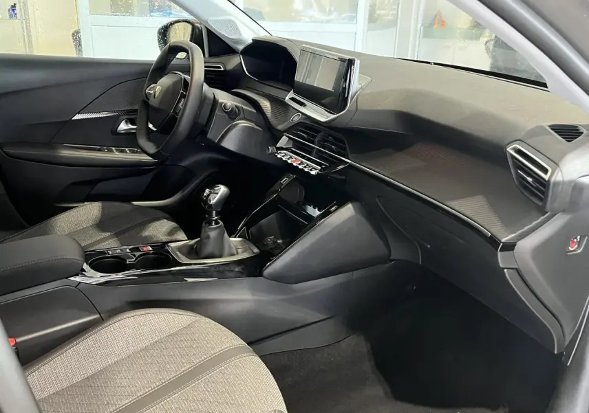 Intérieur avant droit de la Peugeot 208 2024 gris clair avec tableau de bord moderne et boîte manuelle.