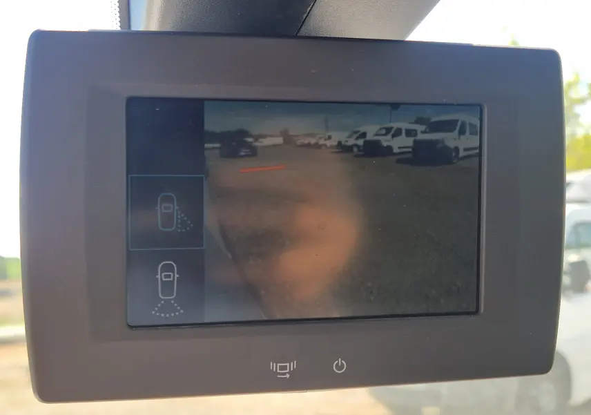 Écran de caméra de recul montrant un parking avec plusieurs véhicules utilitaires blancs, vue depuis l'intérieur du Citroën Berlingo blanc.