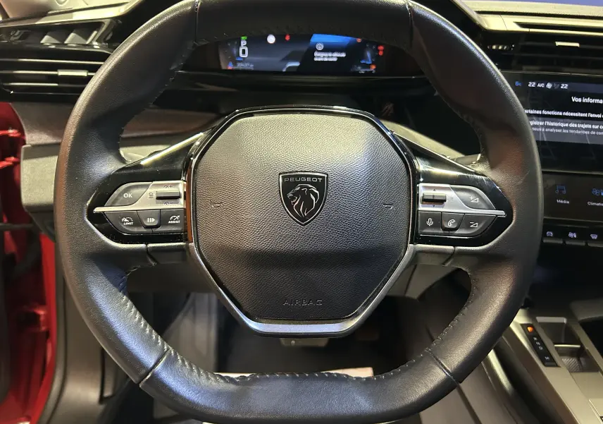 Vue rapprochée du volant cuir noir de la Peugeot 308 rouge 2024 avec commandes intégrées et tableau de bord numérique.