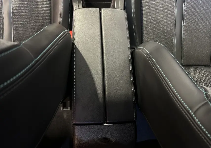 Vue plongeante sur l'accoudoir central noir avec surpiqûres bleues entre les sièges avant d'une Peugeot 308 rouge 2024.