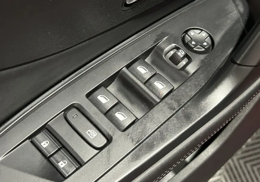 Gros plan sur les commandes des vitres électriques et des rétroviseurs côté conducteur d'une Peugeot 308 rouge 2024.