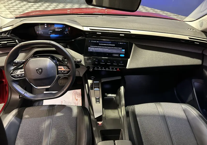 Vue intérieure avant de la Peugeot 308 rouge 2024, mettant en valeur le tableau de bord numérique et l'écran tactile central.