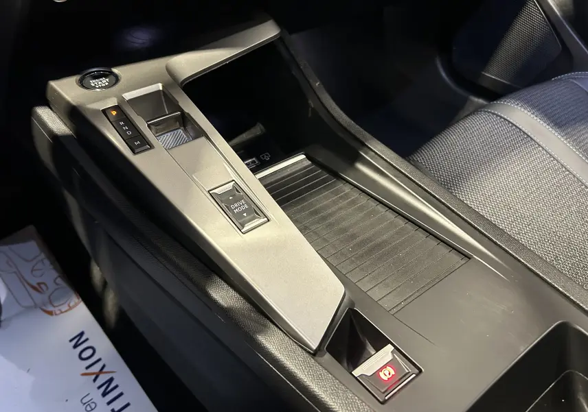 Vue rapprochée de la console centrale grise avec sélecteur de boîte auto et frein à main électrique dans Peugeot 308 rouge 2024.