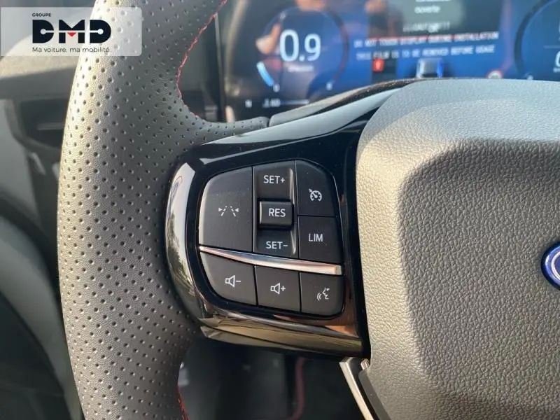 Gros plan sur les commandes multifonctions à gauche du volant perforé avec surpiqûres rouges du Ford Puma gris Cactus.