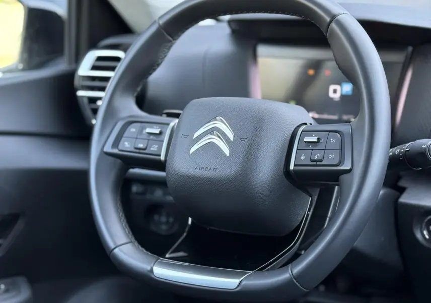 Gros plan sur le volant cuir noir du Citroën C4 X 2024 avec commandes intégrées et logo argenté central.