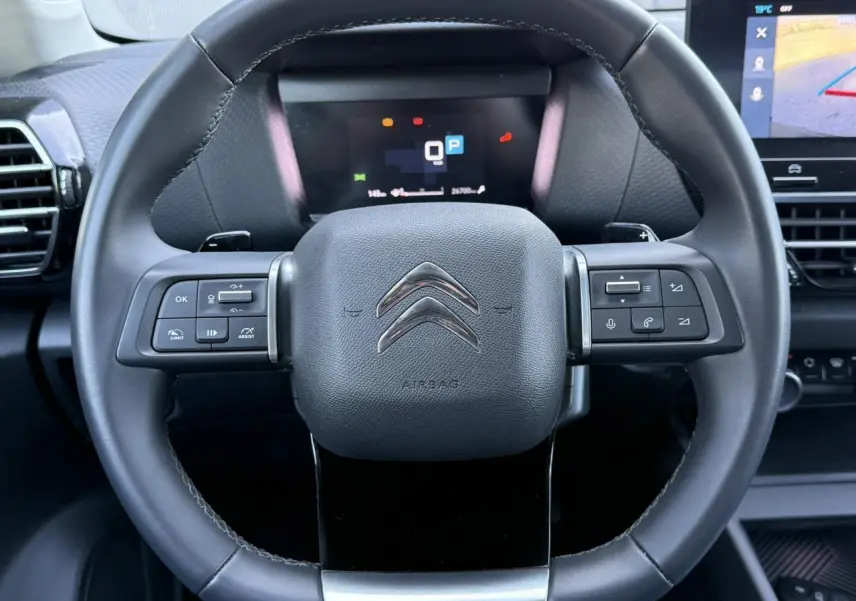 Volant cuir noir de Citroën C4 X 2024 avec commandes intégrées et tableau de bord numérique en arrière-plan.