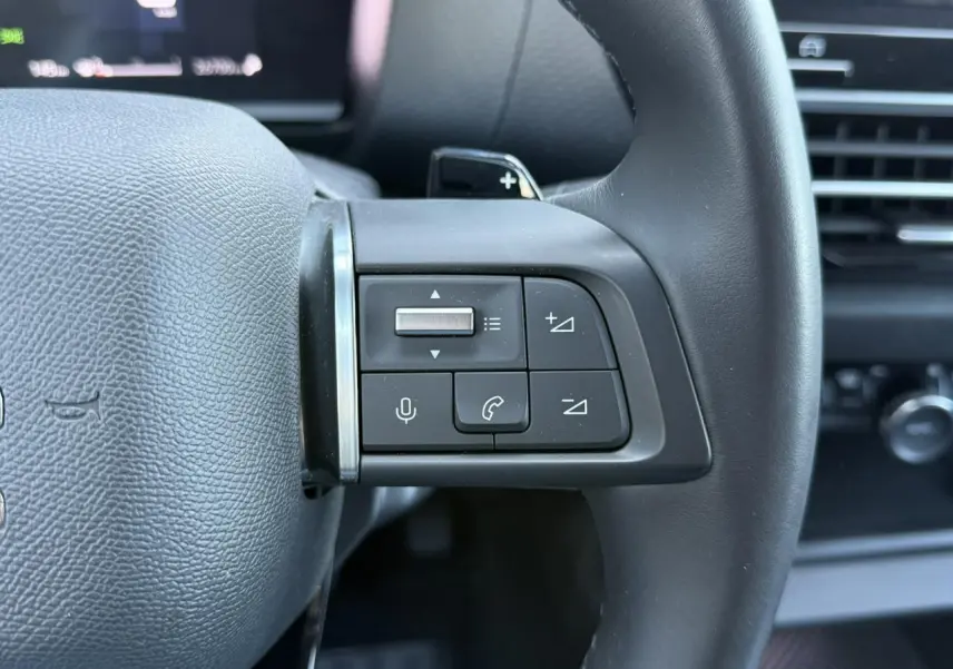 Gros plan sur les commandes audio et téléphone au volant cuir noir du Citroën C4 X 2024, intérieur moderne.