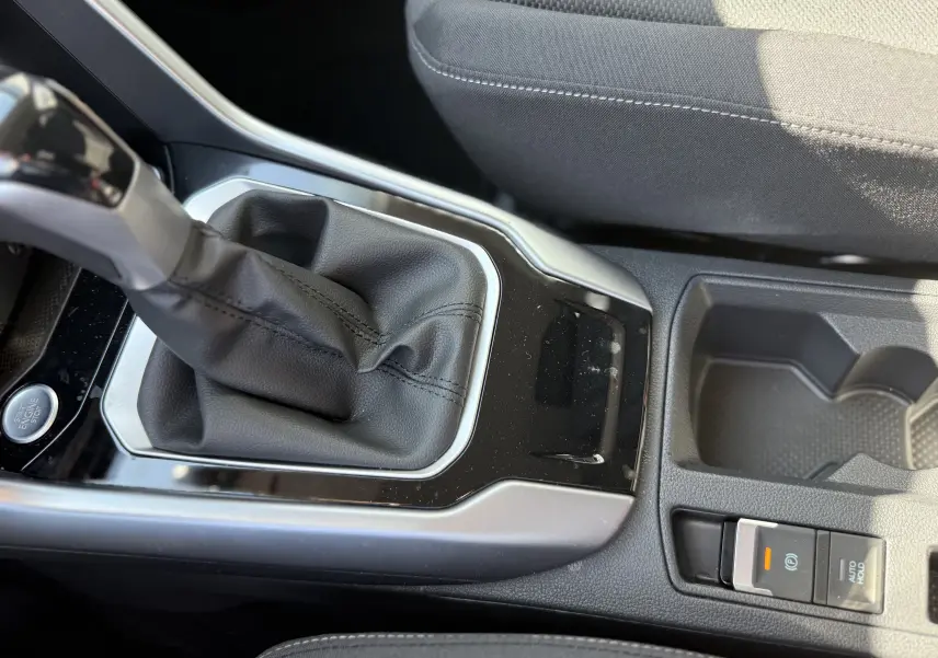 Gros plan sur la console centrale du Volkswagen T-Roc gris pyrite 2025, montrant le levier de vitesse automatique et le frein à main électronique.