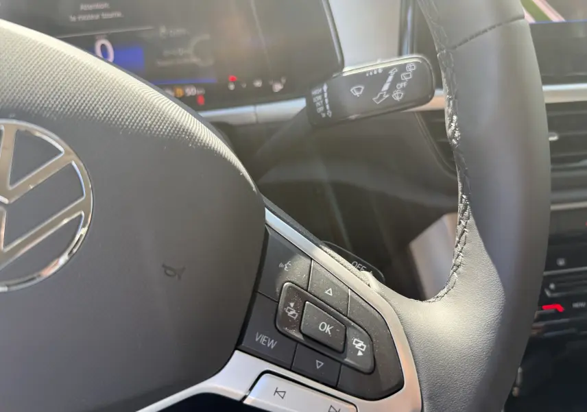 Gros plan sur le volant noir du Volkswagen T-Roc 2025 avec commandes multifonctions et tableau de bord numérique en arrière-plan.