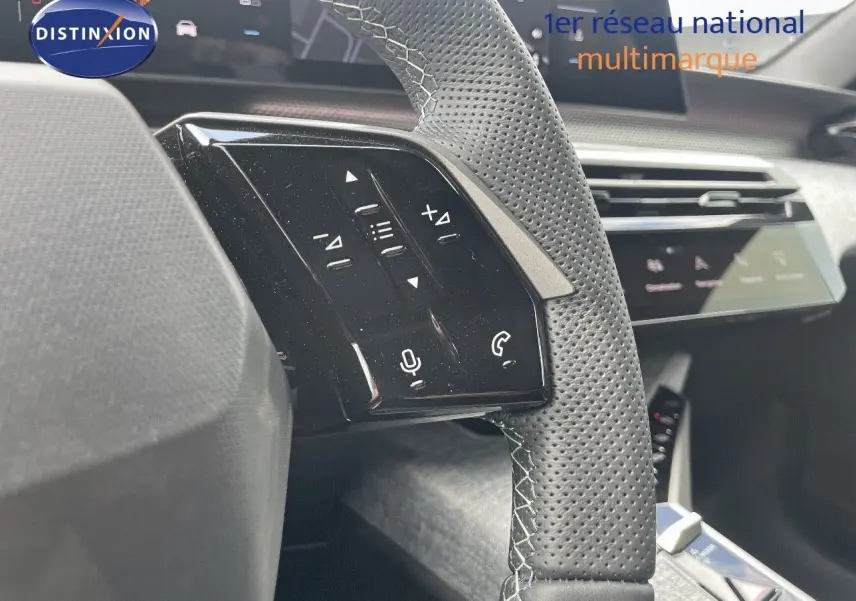 Gros plan sur les commandes gauche du volant perforé en cuir noir du Peugeot 5008 Hybrid 2025, avec tableau de bord en arrière-plan.