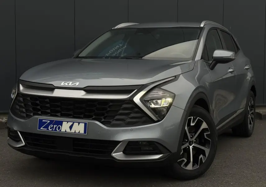 Kia Sportage gris perle en 3/4 avant droit, avec calandre noire et jantes alliage 18 pouces distinctives.