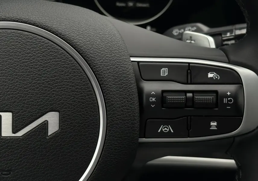Gros plan sur les commandes à droite du volant cuir du Kia Sportage gris perle 2025, avec régulateur adaptatif.