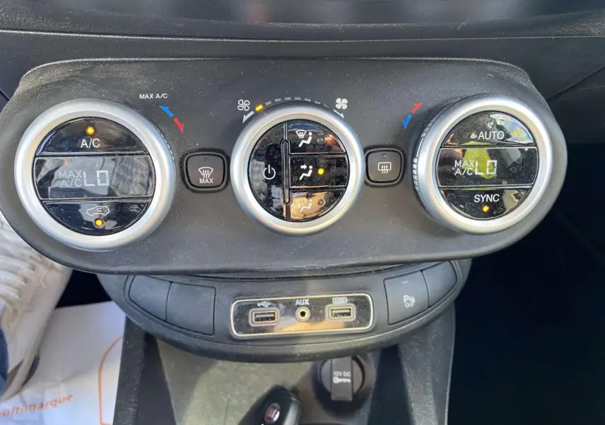 Gros plan sur les commandes de climatisation et les ports USB d'une Fiat 500X noire, version City Cross Business 2019.