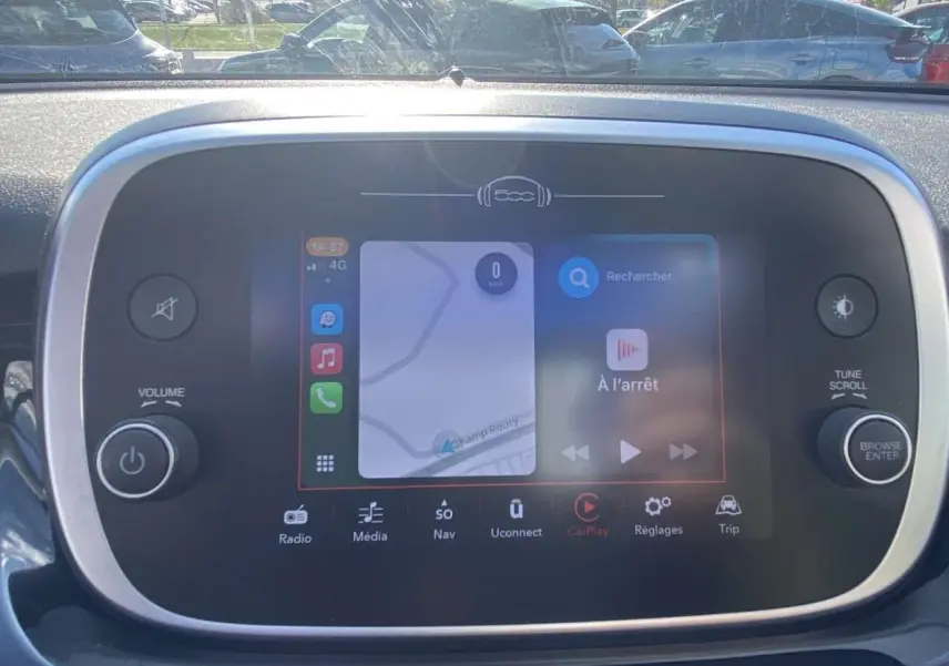 Écran tactile central de la Fiat 500X affichant la navigation et Apple CarPlay, avec commandes autour et reflet extérieur.