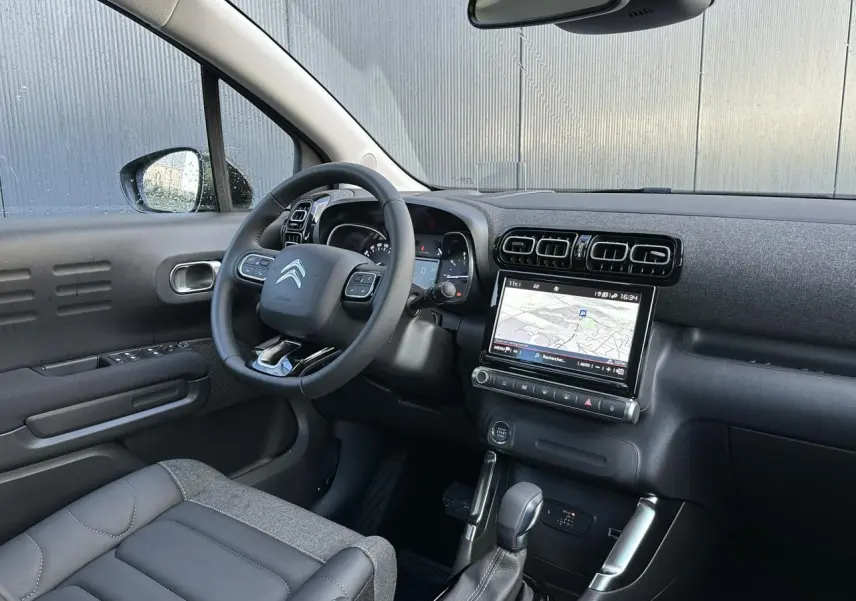 Vue intérieure côté conducteur du Citroën C3 Aircross 2024, montrant le volant, écran GPS tactile et sellerie gris foncé.