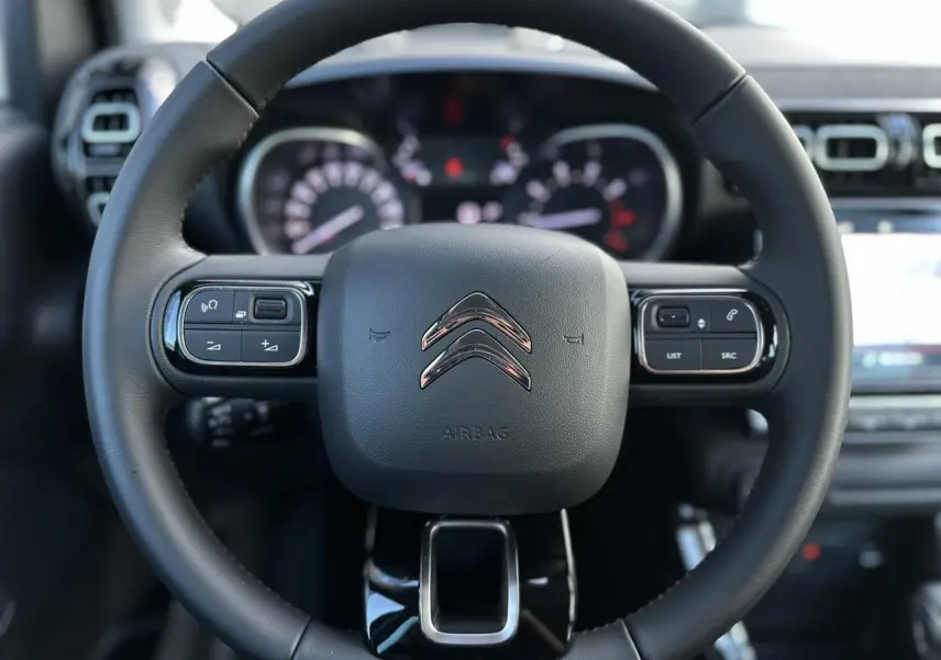 Gros plan sur le volant cuir noir du Citroën C3 Aircross 2024 avec commandes intégrées et tableau de bord flou en arrière-plan.