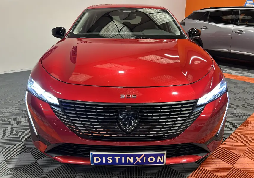 Vue avant d'une Peugeot 308 rouge 2024 avec calandre noire et phares LED allumés dans un showroom.