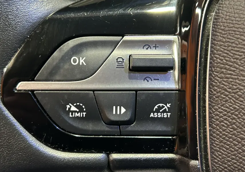 Gros plan sur les commandes de régulateur et limiteur de vitesse au volant d'une Peugeot 308 rouge 2024.