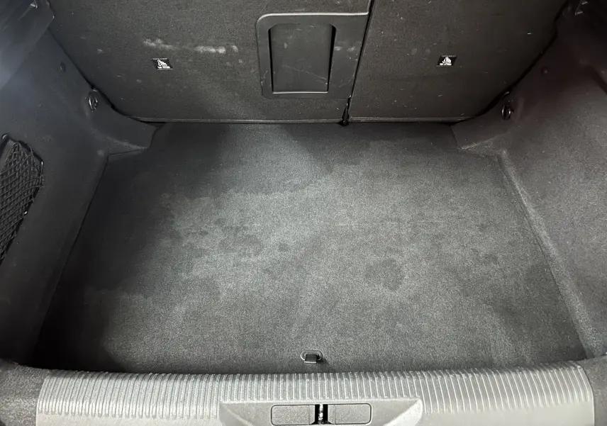 Vue intérieure du coffre vide de la Peugeot 308 rouge 2024, montrant le tapis et les parois en tissu noir.