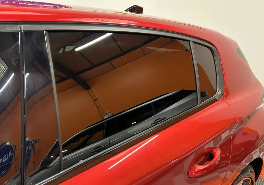 Vue rapprochée du côté gauche arrière d’une Peugeot 308 rouge 2024 avec vitres teintées et poignée de porte visible.