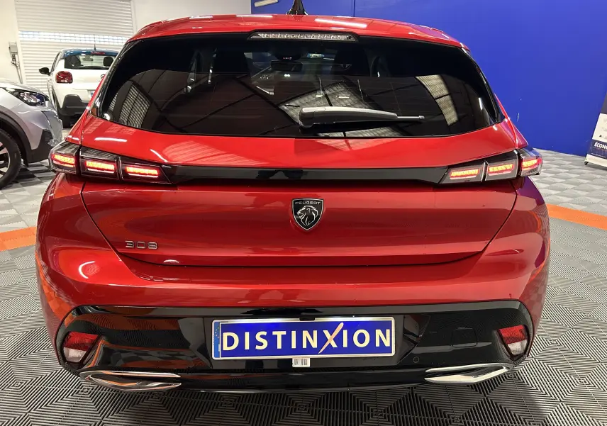 Vue arrière d'une Peugeot 308 rouge 2024 avec feux LED allumés et détails noirs brillants sur le pare-chocs.