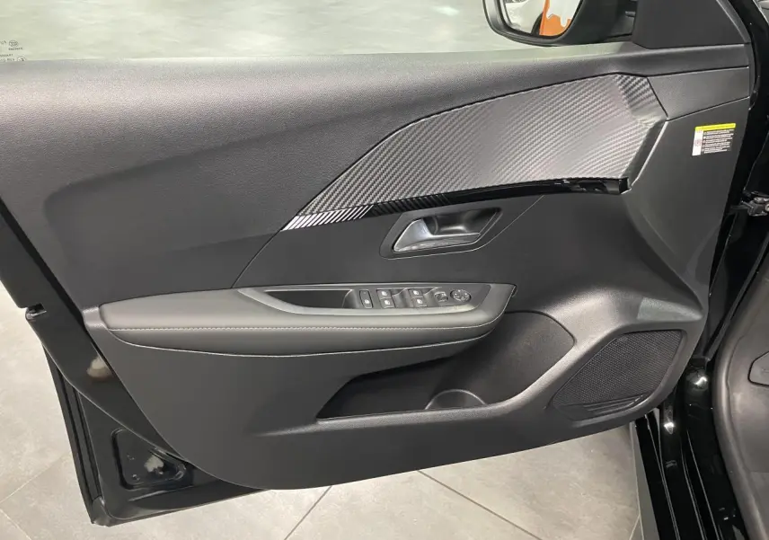 Vue intérieure du panneau de porte avant gauche noir avec insert effet carbone et commandes des vitres électriques sur Peugeot 208 2025.