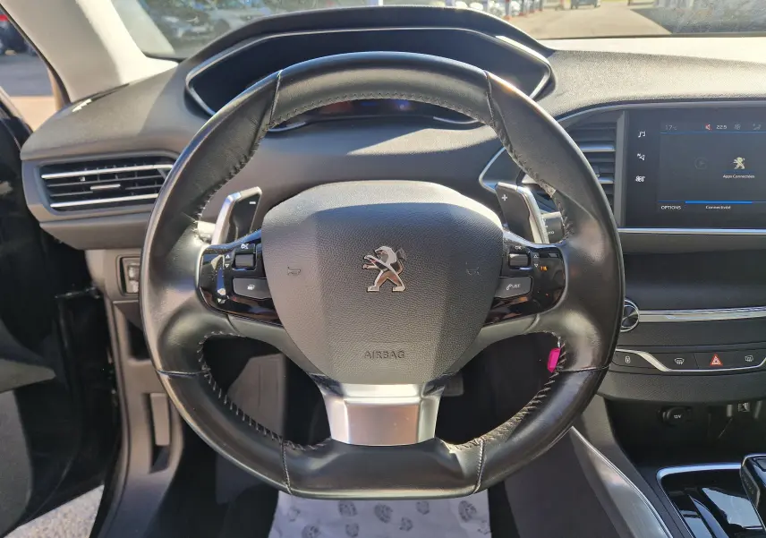 Vue rapprochée du volant cuir noir avec palettes de la Peugeot 308 SW 2021, tableau de bord et écran tactile visibles.