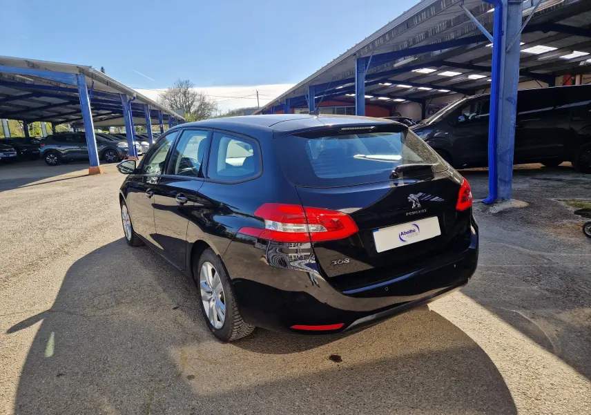 Vue 3/4 arrière droite d'une Peugeot 308 SW noire de 2021 stationnée sous un abri en extérieur.