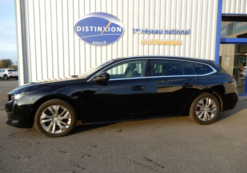 Peugeot 508 SW noir Perla Nera vue de profil côté gauche, stationnée devant un bâtiment avec enseigne Distinxion.