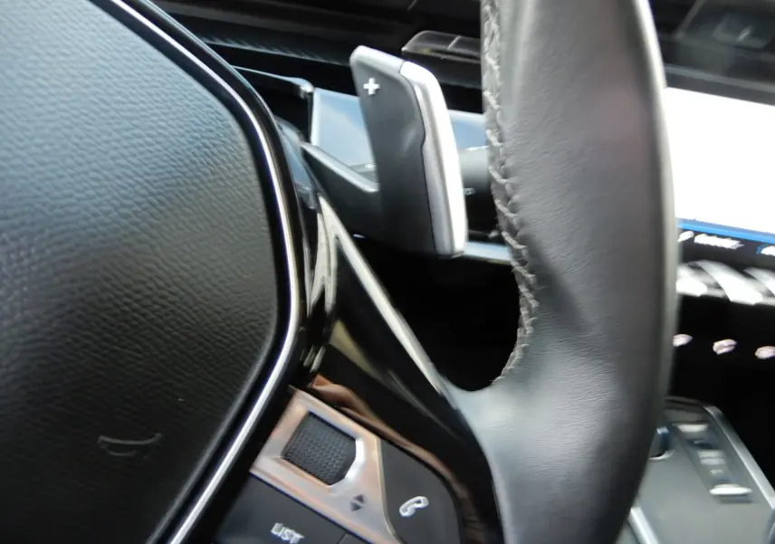 Gros plan sur la palette de changement de vitesse droite et partie du volant en cuir noir du Peugeot 508 SW noir Perla Nera.