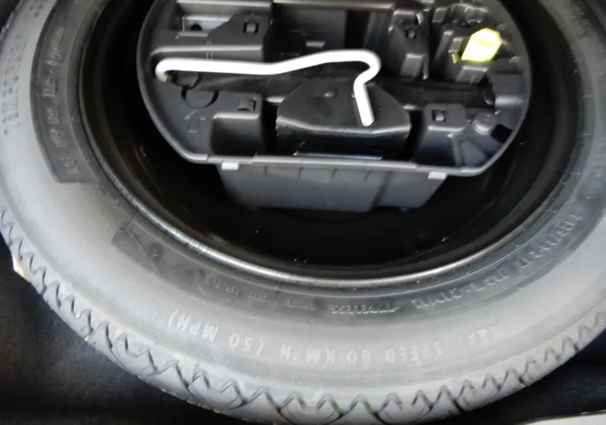 Gros plan sur la roue de secours et la boîte à outils noire dans le coffre d'une Peugeot 508 SW noire.