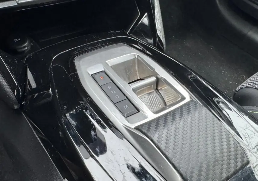 Gros plan sur la console centrale noire brillante de la Peugeot 208 Hybrid 110 e-DCS6 GT avec levier de vitesses automatique.
